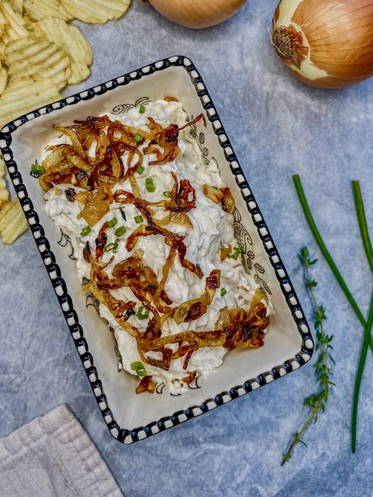 Caramelized french onion dip in a dish with some chips, chives, and onions scattered around