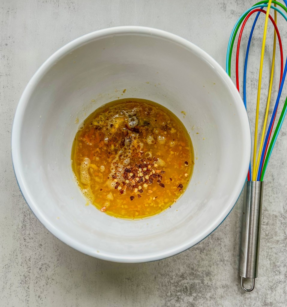 Honey citrus dressing in a mixing bowl with a whisk next to it