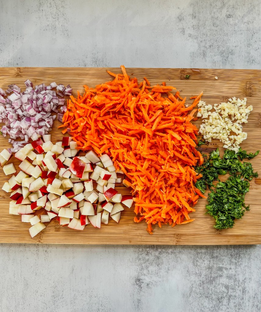 Carrots, apple, red onion, garlic, and cilantro prepped on a cutting board