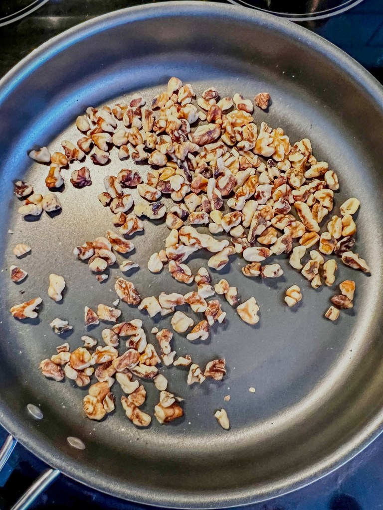 Chopped walnuts being toasted in a skillet on the stove