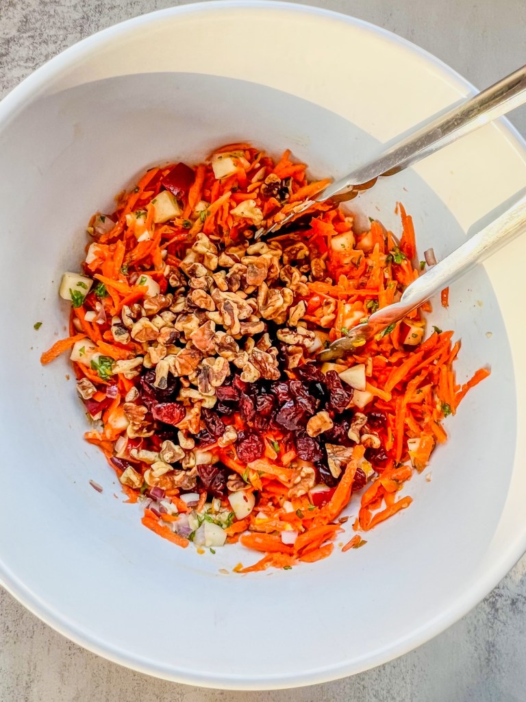 Carrot salad in a bowl being tossed with a citrus honey dressing with a tong