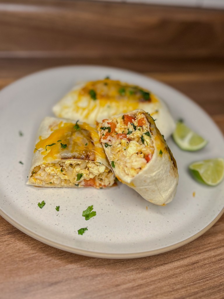 Cheesy Chicken Burrito cut in half with another burrito next to it on a white plate with some lime wedges