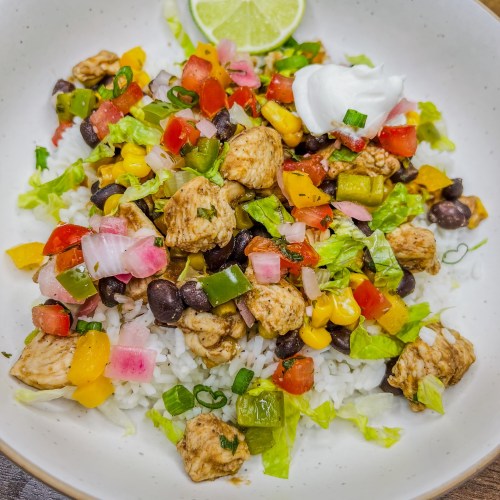 Chicken Burrito Bowl in a white bowl with sour cream, herbs, and lime for garnish