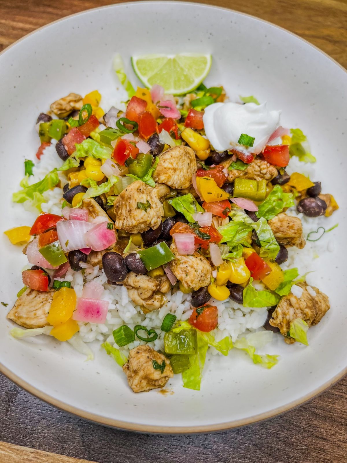 Chicken Burrito Bowl in a white bowl with sour cream, herbs, and lime for garnish