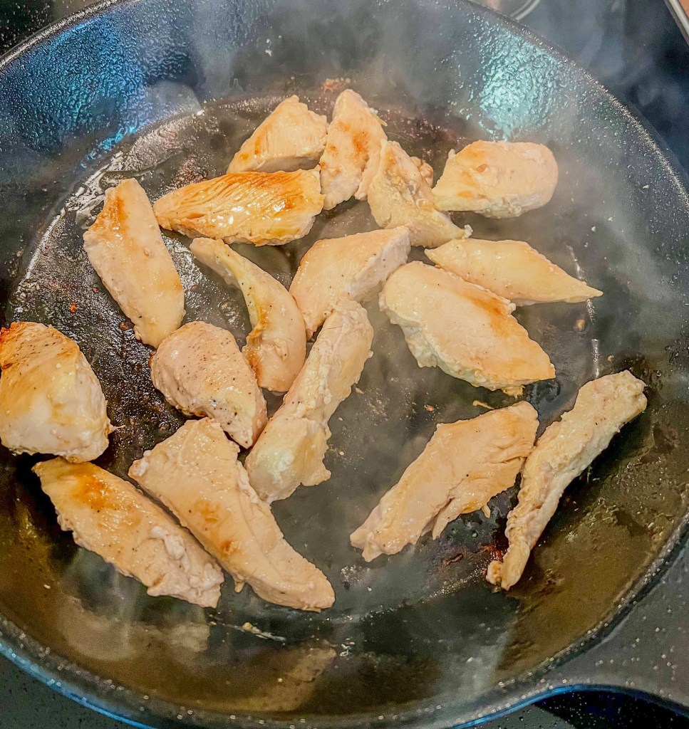 Chicken cut into tenders, cooking in a skillet on the stove
