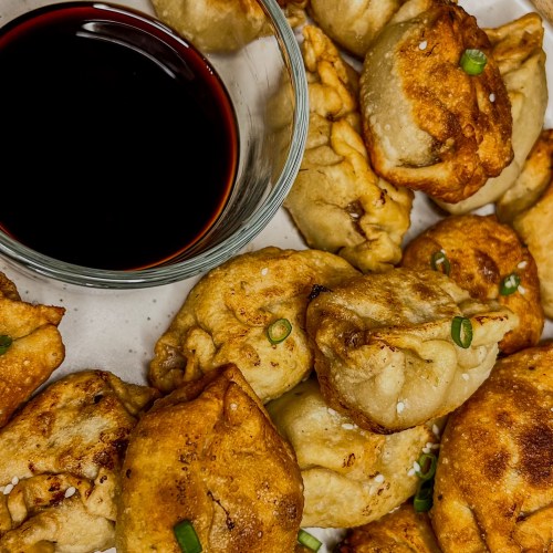 Chinese dumplings on a white plate with a small dish of soy sauce next to it