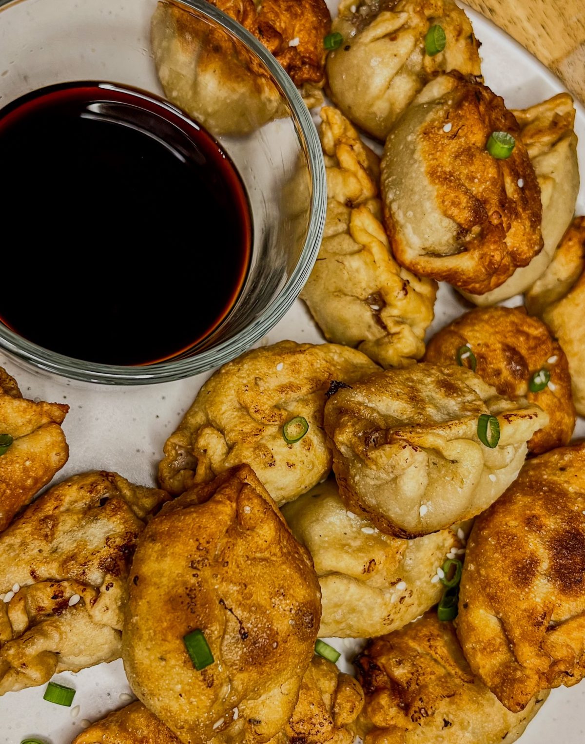 Chinese dumplings on a white plate with a small dish of soy sauce next to it