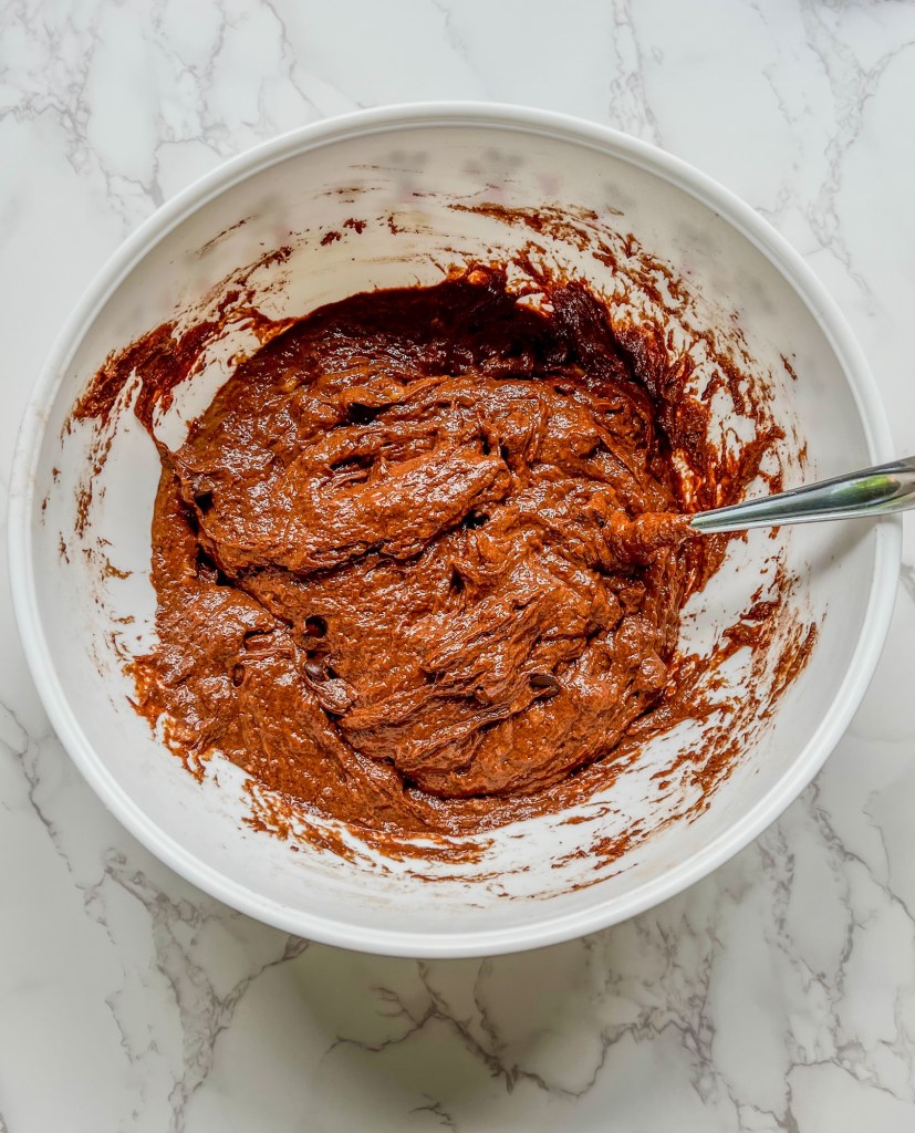 Batter for chocolate banana muffins in a bowl with a spoon inside of it