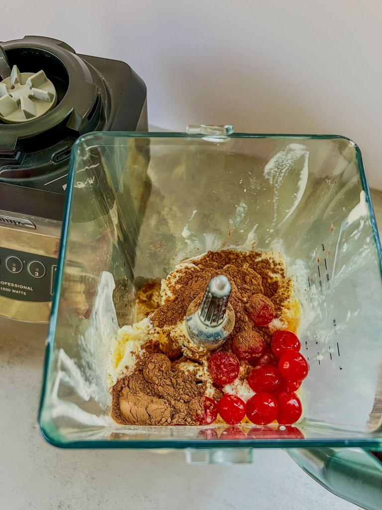 Cherries, cocoa powder, ice cream, coffee, and cream in a blender