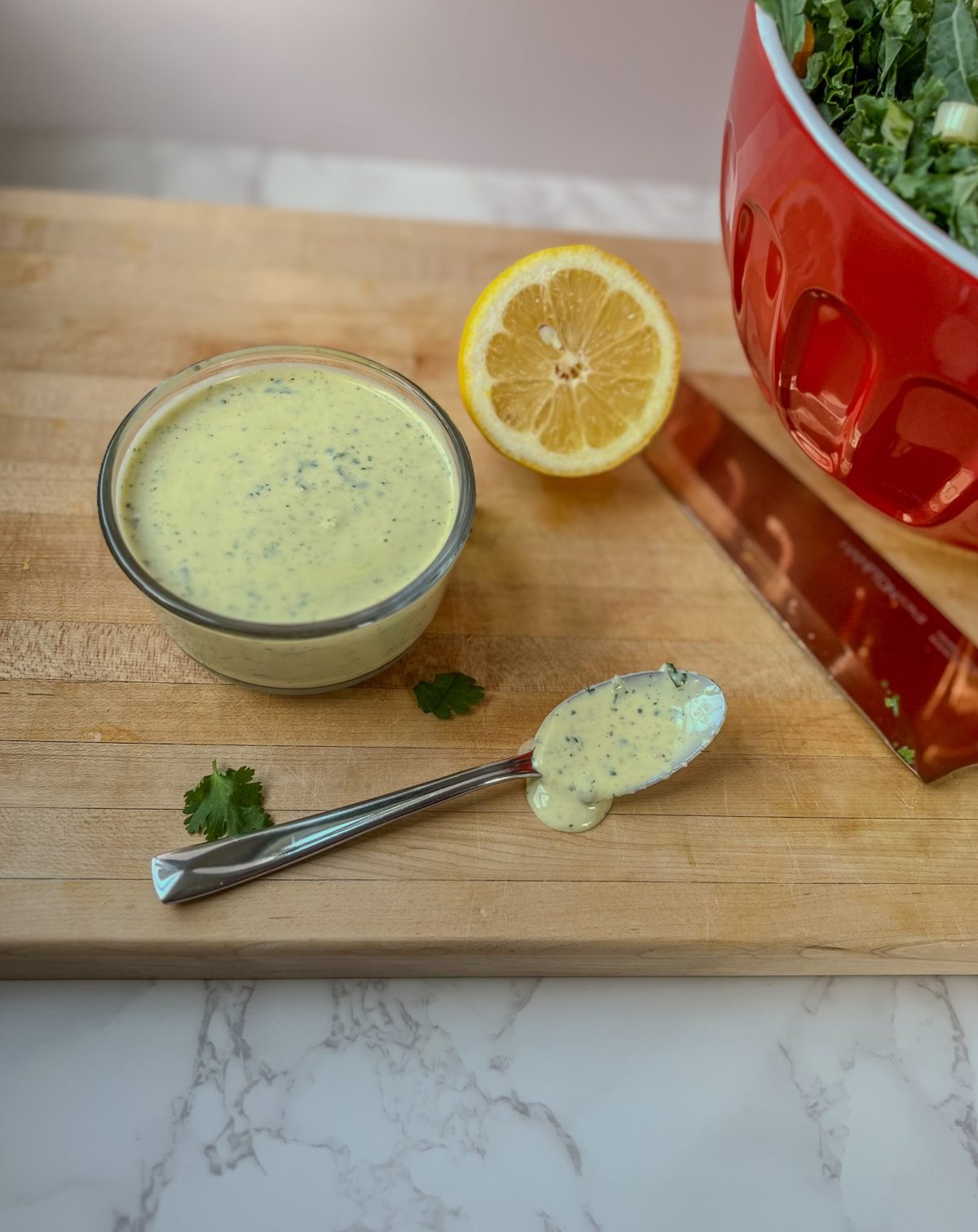 Cilantro lemon dressing in a glass dish on a wooden cutting board with a spoonful of it nearby