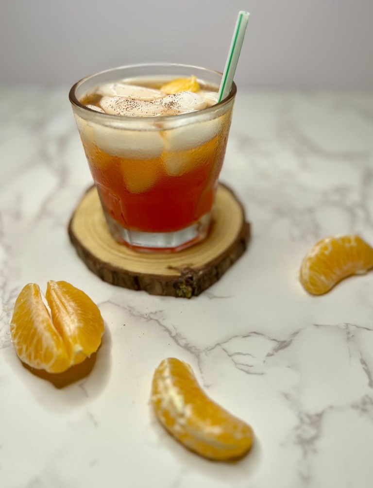 A clementine bourbon refresher in a short glass with a straw and some clementine wedges near it