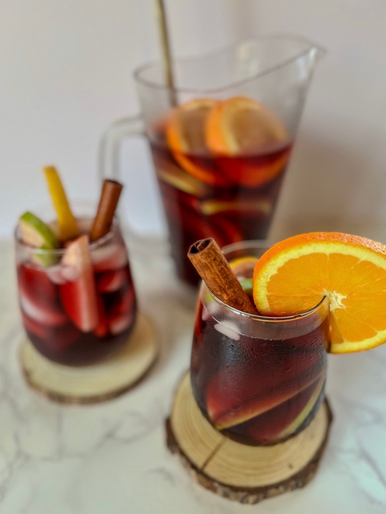 Two glasses of cranberry sangria with a large pitcher behind