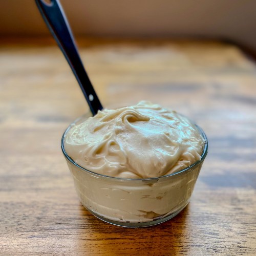 Cream cheese frosting in a glass dish with a rubber spatula sticking out of it, on a wooden table