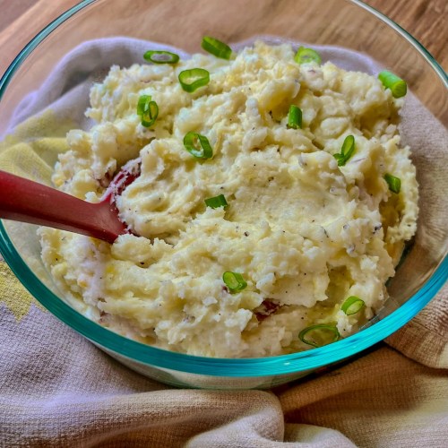 Creamy mashed potatoes in a glass dish with green onion on top and a red serving spoon inside