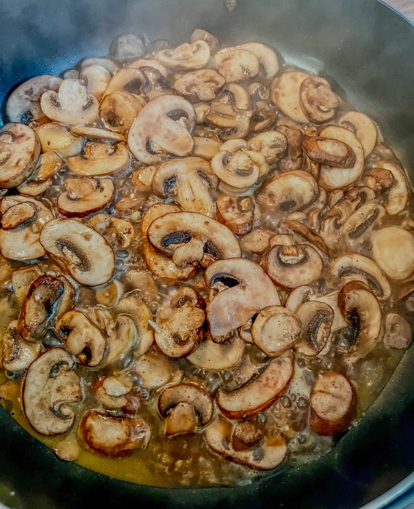 Baby bella mushrooms being cooked in a large skillet on the stove