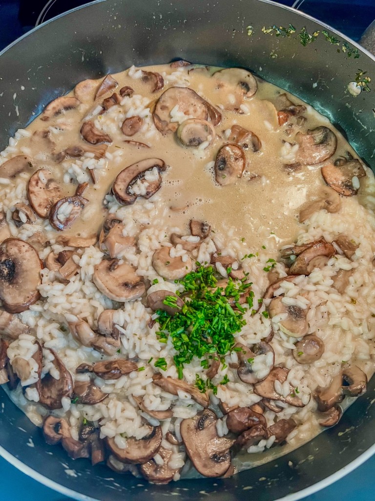 Rice, mushroom, garlic, chive, broth, and wine all coming together in a skillet to make a risotto