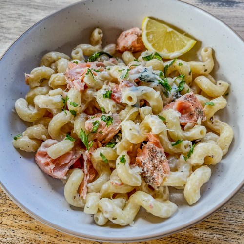 Creamy Salmon Pasta in a white bowl with parsley and lemon wedges for garnish on a wooden table