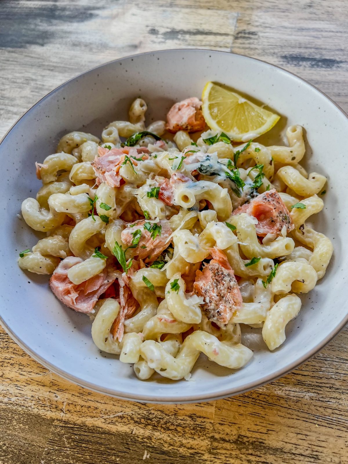 Creamy Salmon Pasta in a white bowl with parsley and lemon wedges for garnish on a wooden table