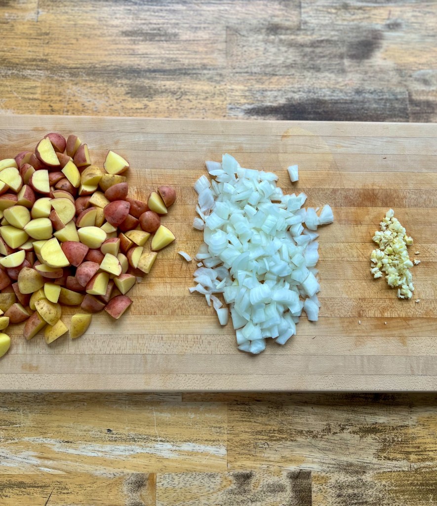 Potato, onion, and garlic that's been chopped up on a cutting board