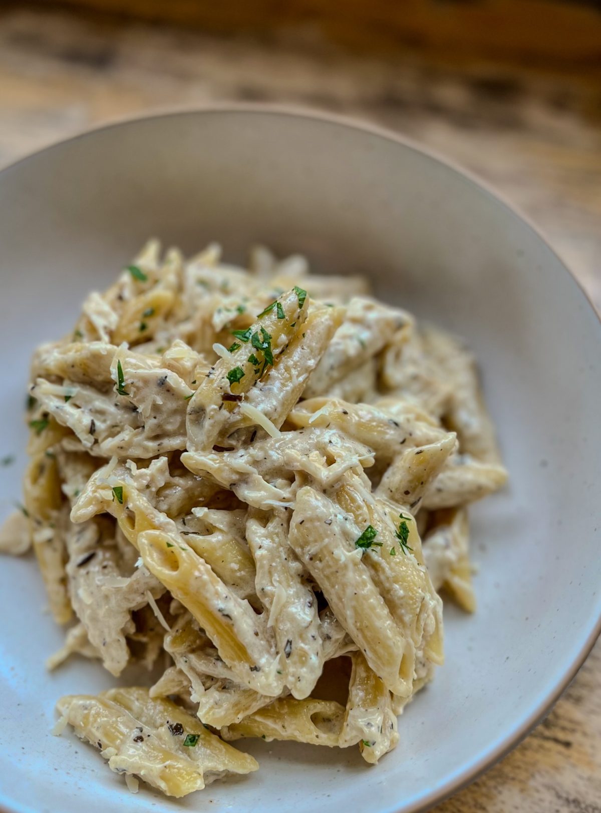 Crockpot Chicken Alfredo in a white bowl with some parsley and parmesan on top, on a table