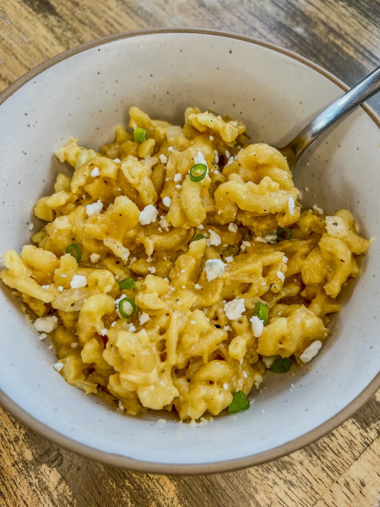 Crockpot mac and cheese in a white bowl with a spoon inside, on a wooden table