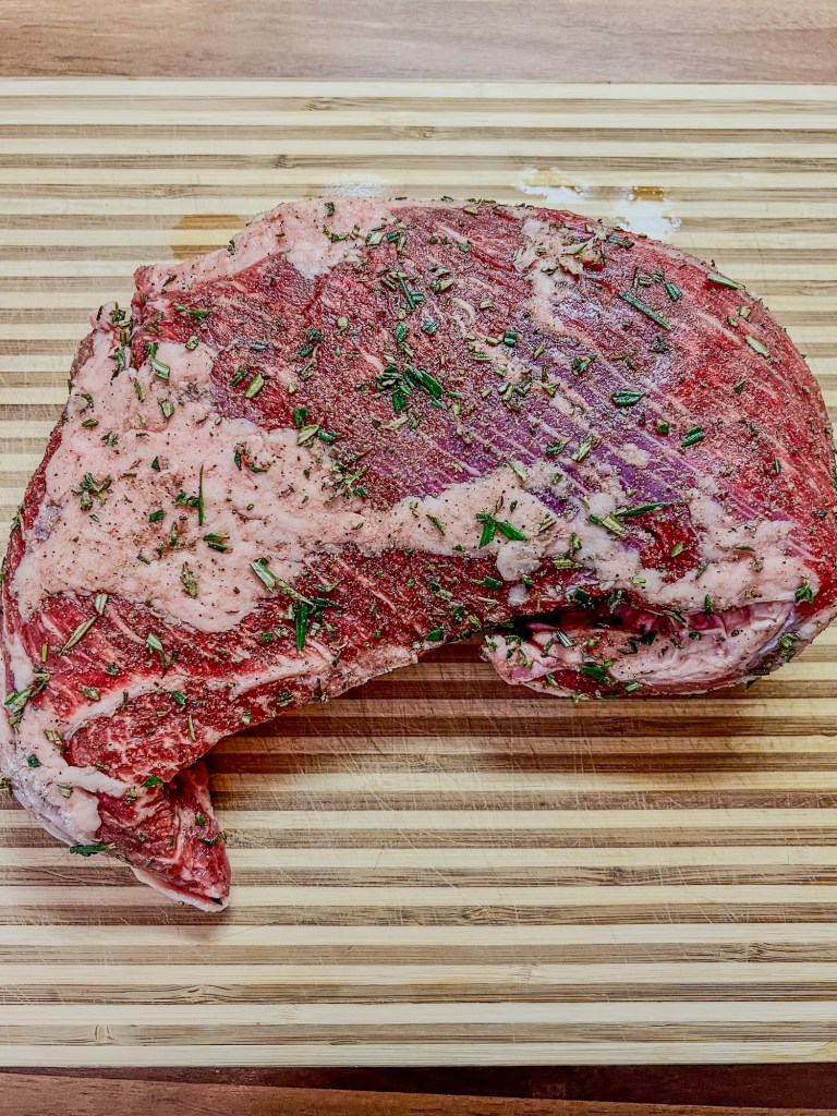 Snake River Farms tri-tip with herbs and seasonings on it on a wooden cutting board