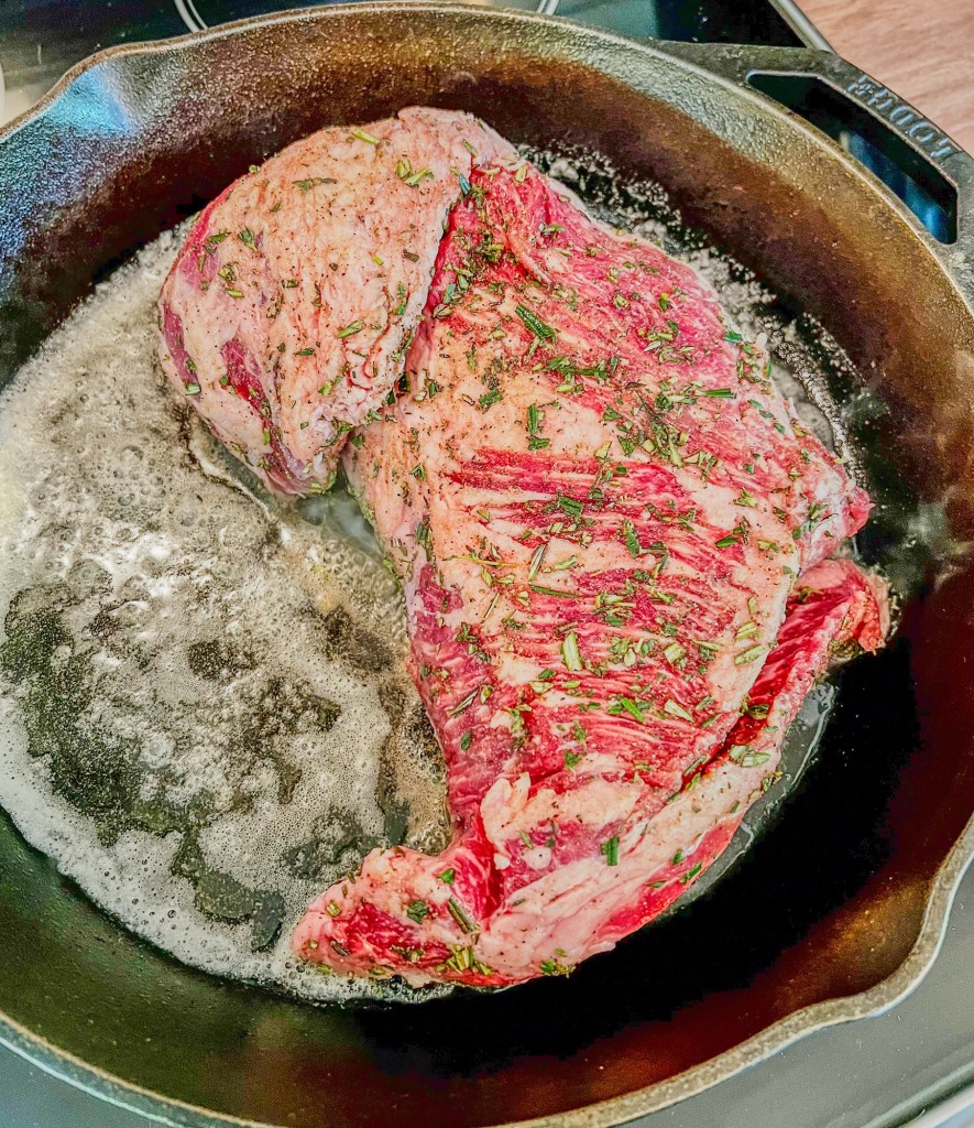 Tri-tip cooking in a cast iron skillet on the stove