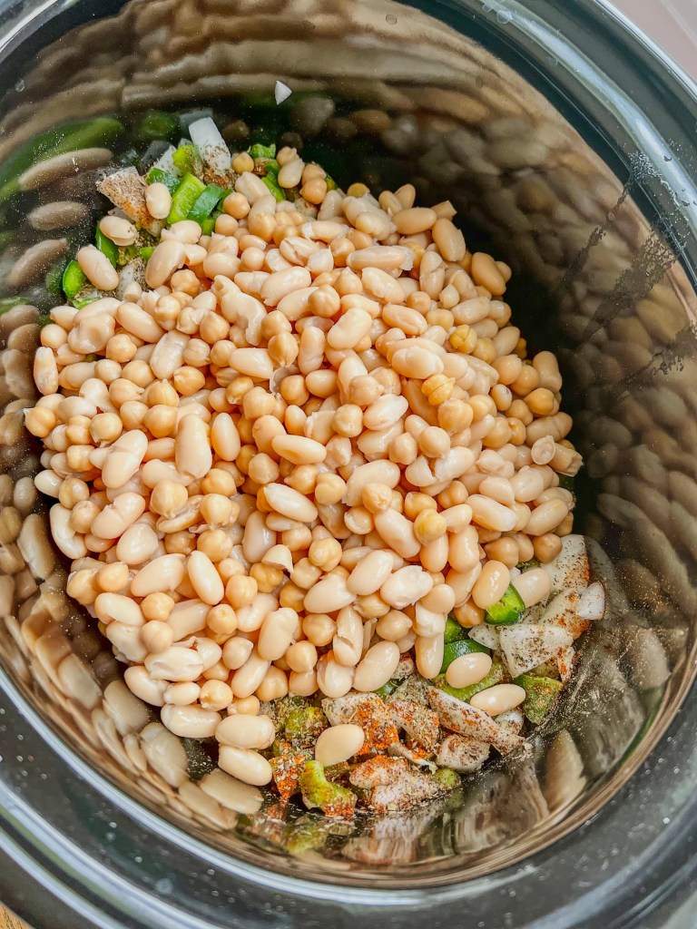 A crockpot filled with veggies, chicken, seasonings, and beans