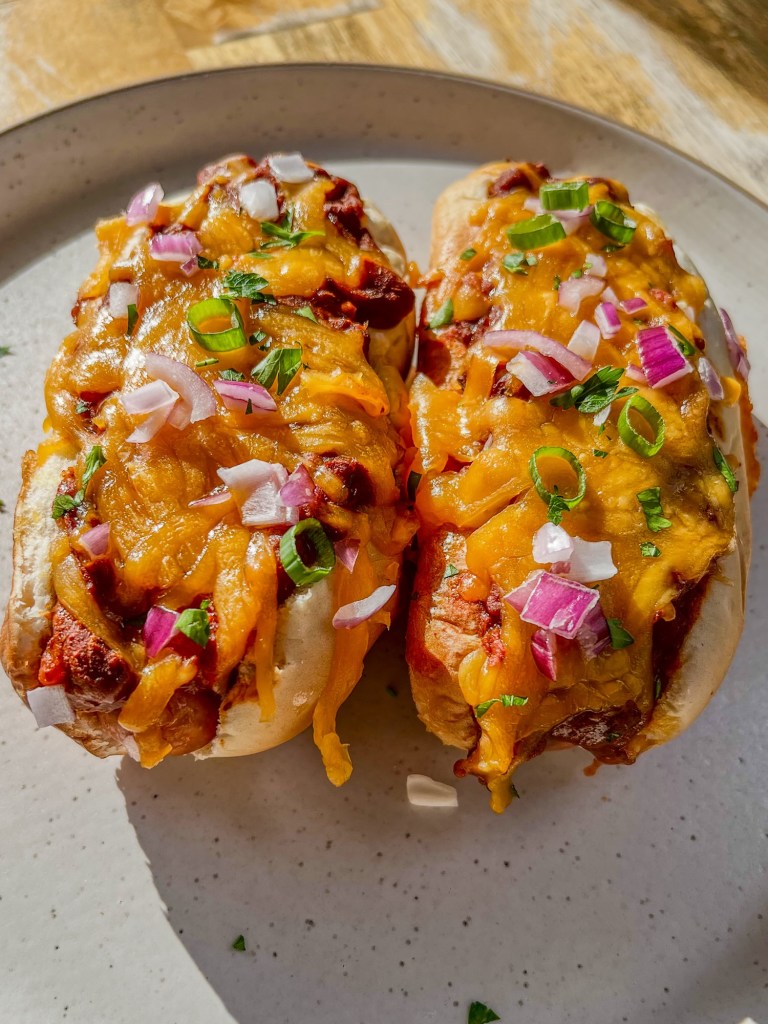 Chili cheese dogs on a white plate on a wooden table