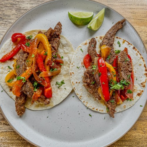 Flank Steak Fajitas on a white plate on a wooden table