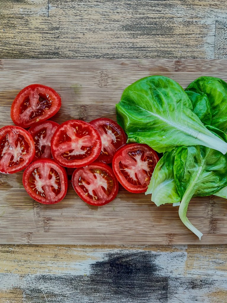 Thinly sliced vine tomatoes with fresh hydroponic lettuce next to it on a cutting board