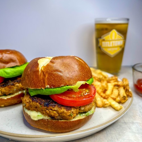 Green onion turkey burgers on a pretzel bun with tomato, lettuce, and honey mustard mayo on a plate with some fries, ketchup, and beer next to it