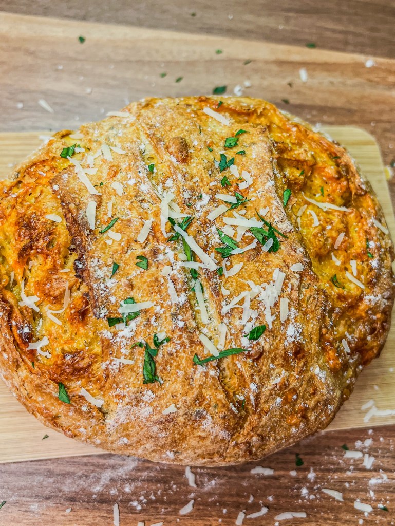 Herb and Cheese bread fresh out of the oven on a wooden cutting board with some garnishes on top