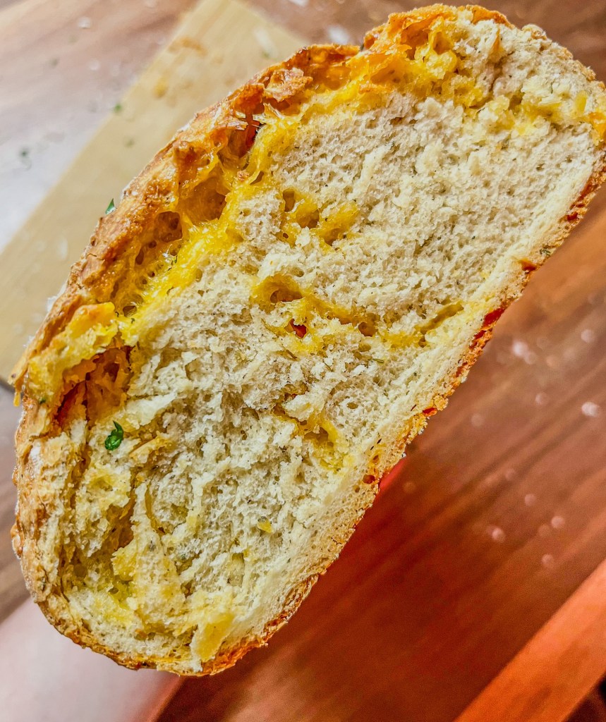 Herb and cheese bread that's been sliced to show the middle and a hand holding it up
