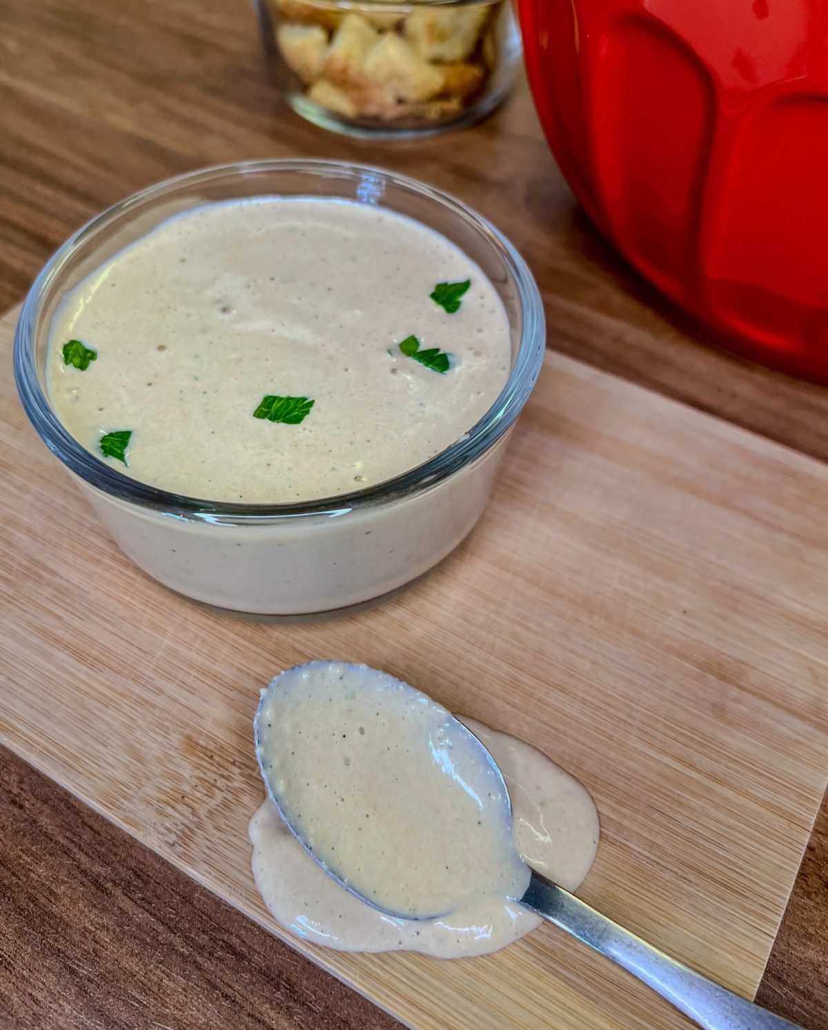 Homemade Caesar Dressing in a small glass dish on a wooden cutting board with a spoonful of it nearby