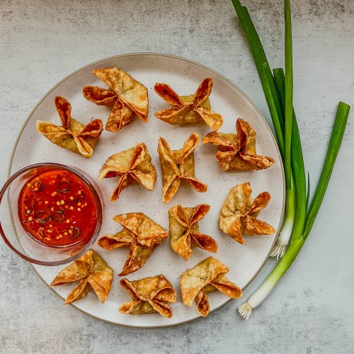 Homemade crab rangoons on a plate with some spicy sweet chili sauce on the side