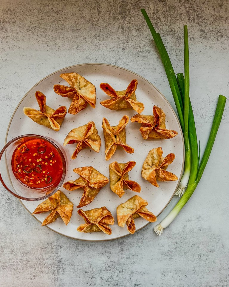 Homemade crab rangoons on a plate with some spicy sweet chili sauce on the side