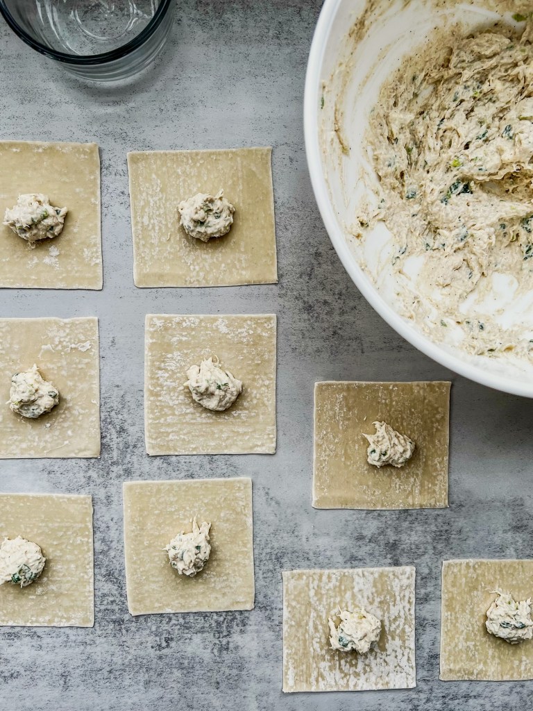 Wonton wrappers with filling scooped onto them, on a countertop