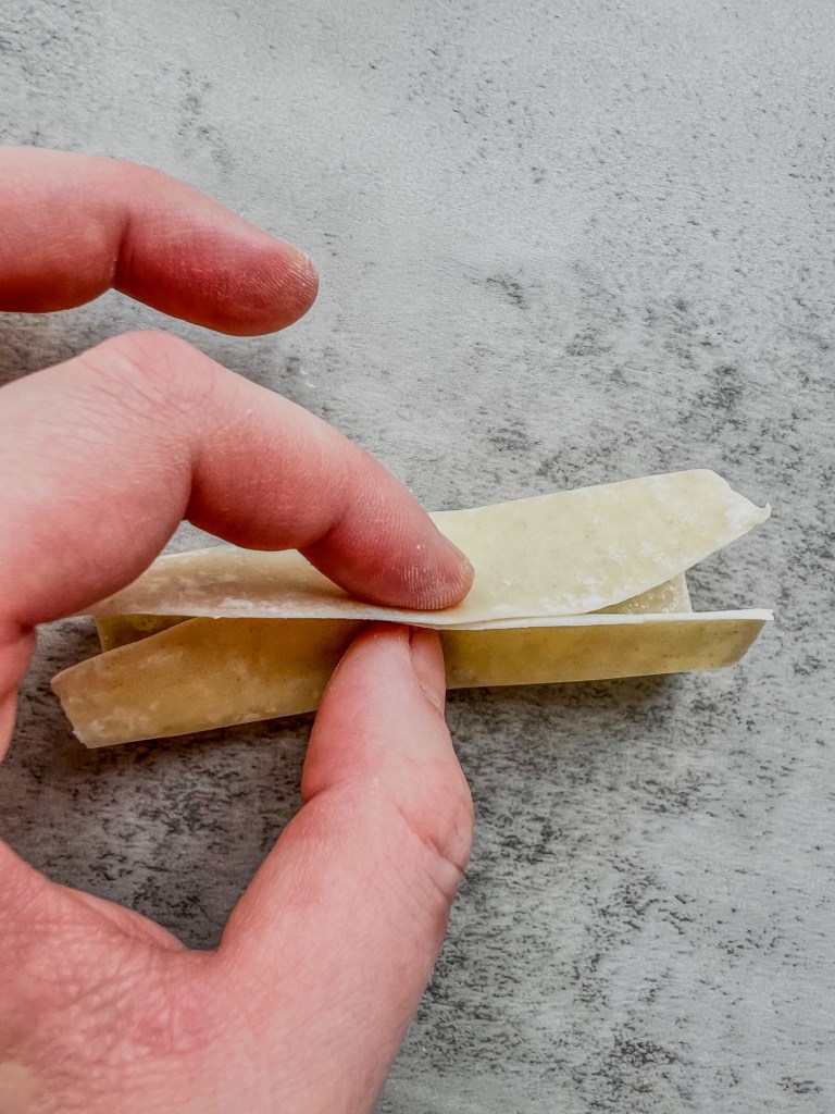 A hand wrapping some filling in a wonton wrapper