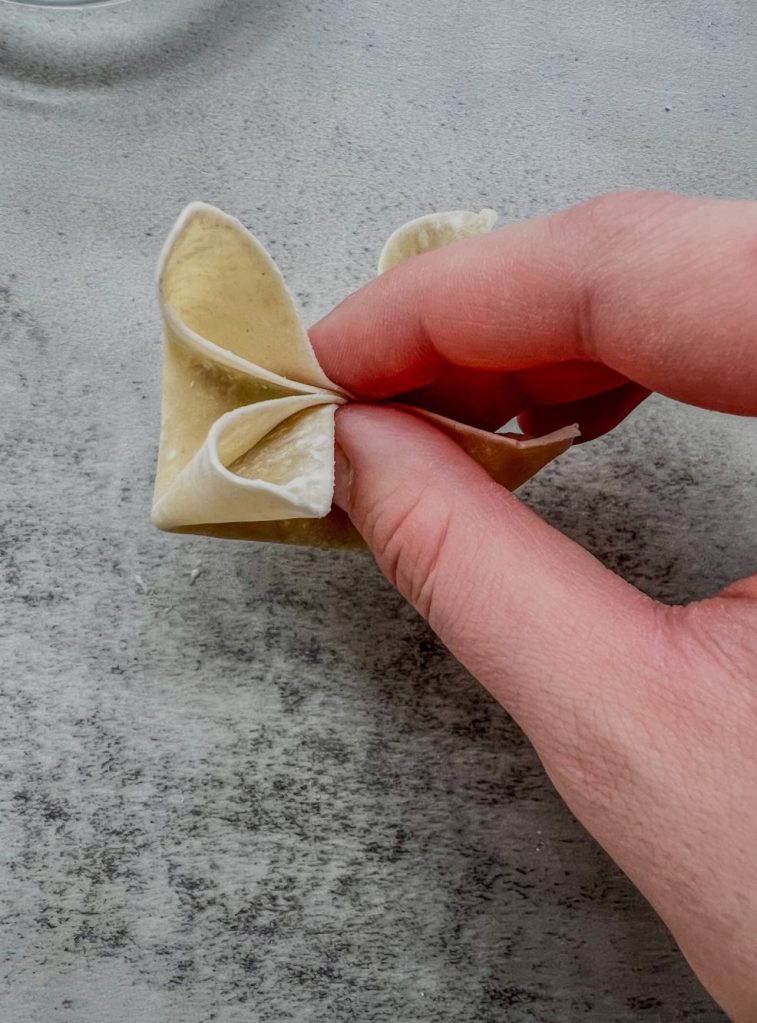 A hand wrapping up a crab rangoon