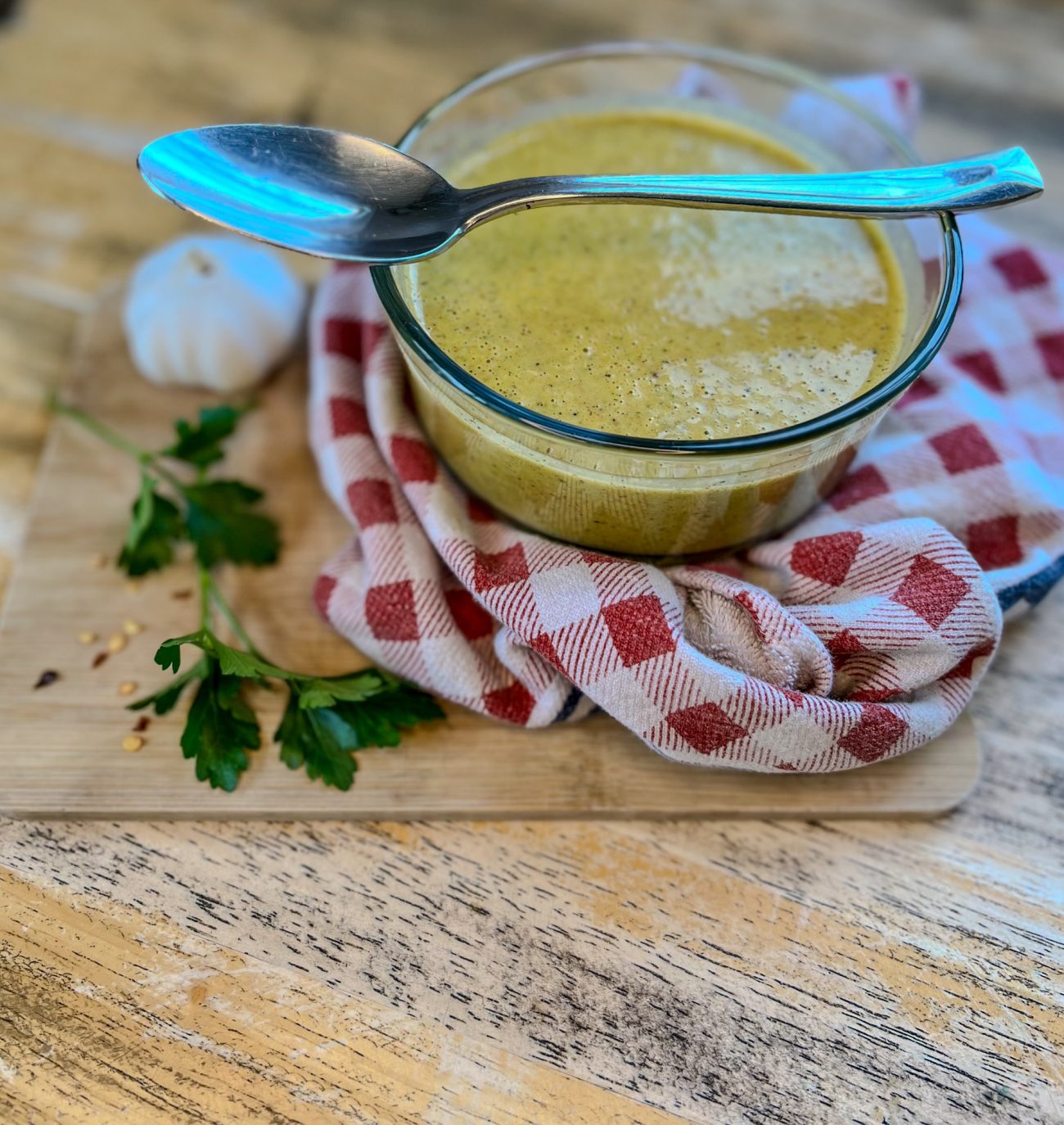 Homemade Italian Dressing in a dish with herbs and garlic next to it, on a table