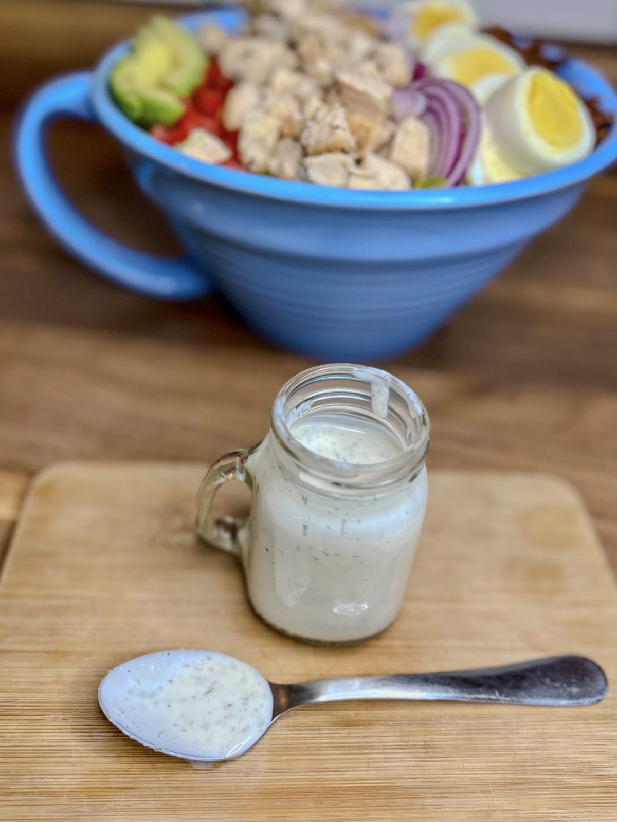 Homemade ranch in a small glass jar with a spoonful of it in front of it and a big salad behind
