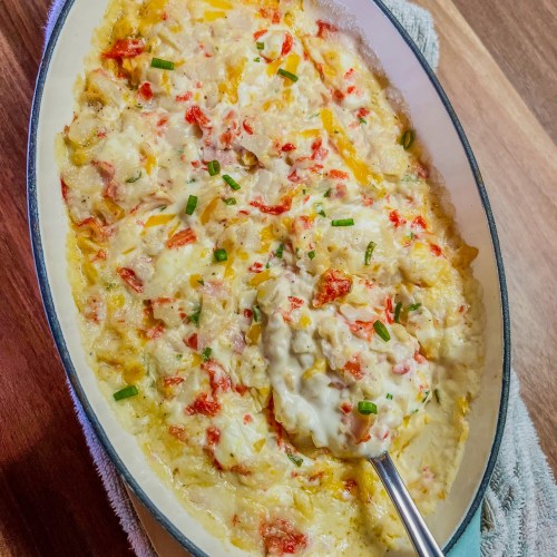 Hot crab dip in a baking dish with a spoon inside on a wooden counter