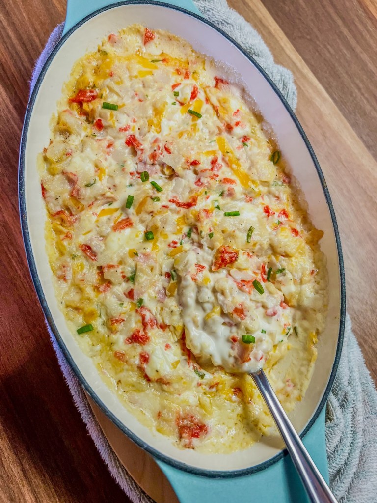 Hot crab dip in a baking dish with a spoon inside on a wooden counter