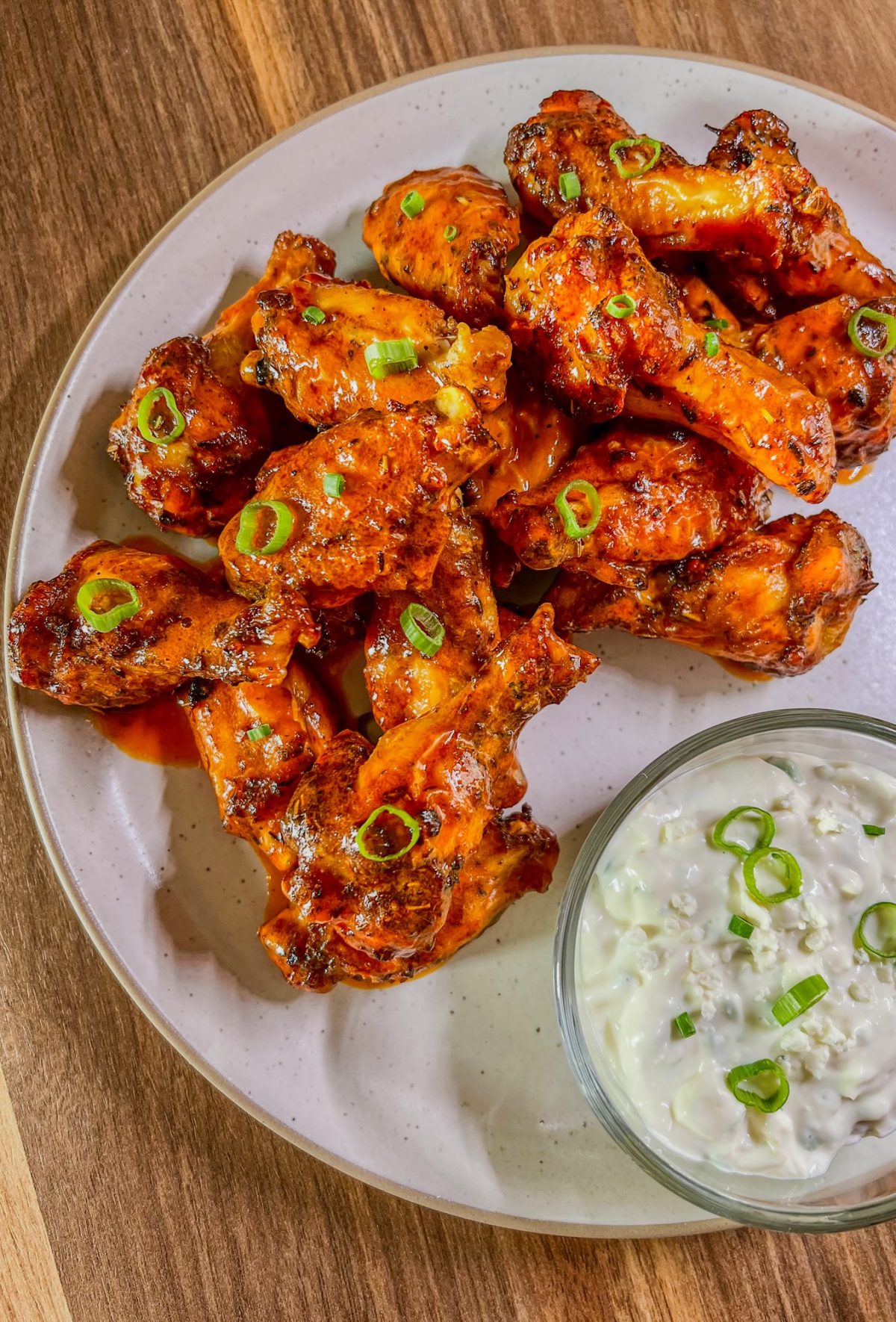 Hot wings on a white plate with blue cheese dressing in a dish next to it