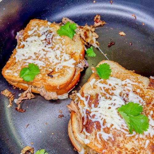 Pulled Pork Grilled Cheese sandwiches with cheese and cilantro on top in a skillet on the stove