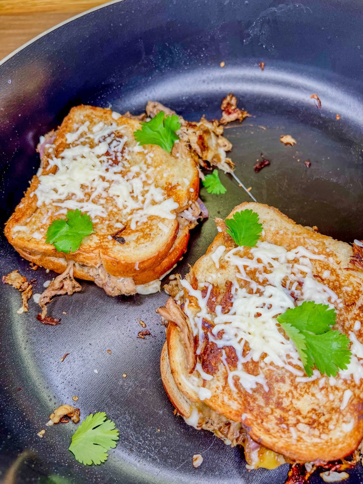 Pulled Pork Grilled Cheese sandwiches with cheese and cilantro on top in a skillet on the stove
