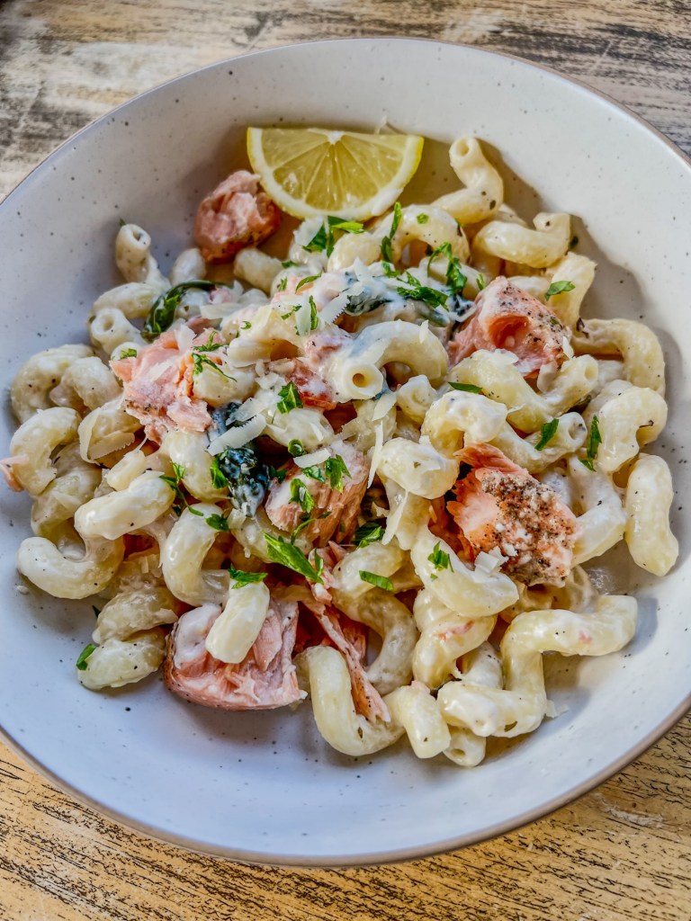 Creamy Salmon Pasta in a white bowl with parsley and lemon wedges for garnish on a wooden table