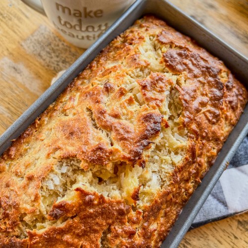 Tropical Banana Bread in a loaf pan on a hot pad, sitting on a wooden table