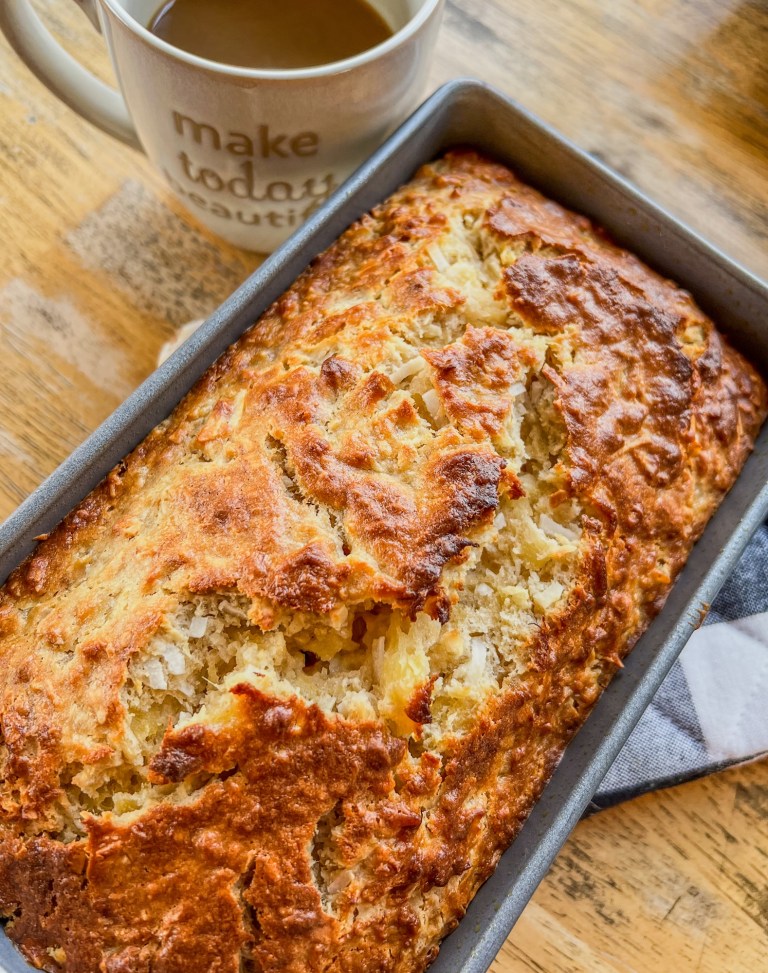 Tropical Banana Bread in a loaf pan on a hot pad, sitting on a wooden table